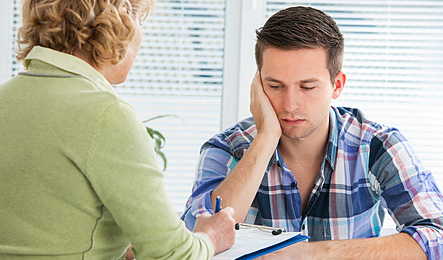 Yngre man och en kvinna sitter mittemot varandra vid ett bord. Kvinnan antecknar. Foto. iStock 