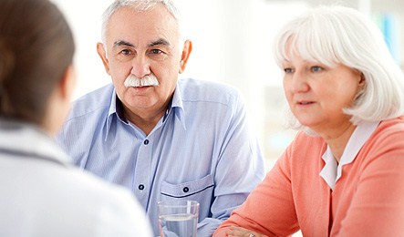 Äldre par samtalar med person i vita kläder. Foto: iStock 