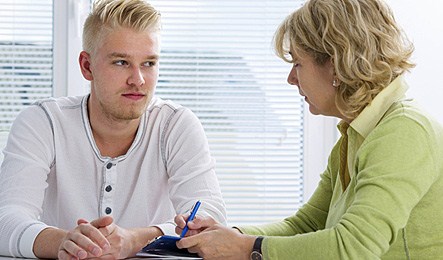 Yngre man och en kvinna sitter mittemot varandra vid ett bord. Kvinnan antecknar. Foto: iStock 