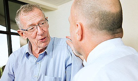 Äldre herre i glasögon samtalar med en man som sitter mittemot, mannen håller sin hand på herrens axel. Foto: iStock 